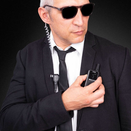 Uomo di sicurezza utilizza radio Midland 777 Pro indossando occhiali da sole e abito scuro.